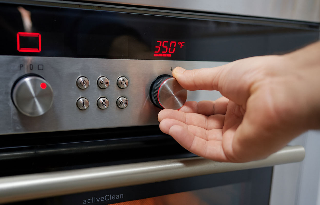A person adjusting the temperature dial on an oven